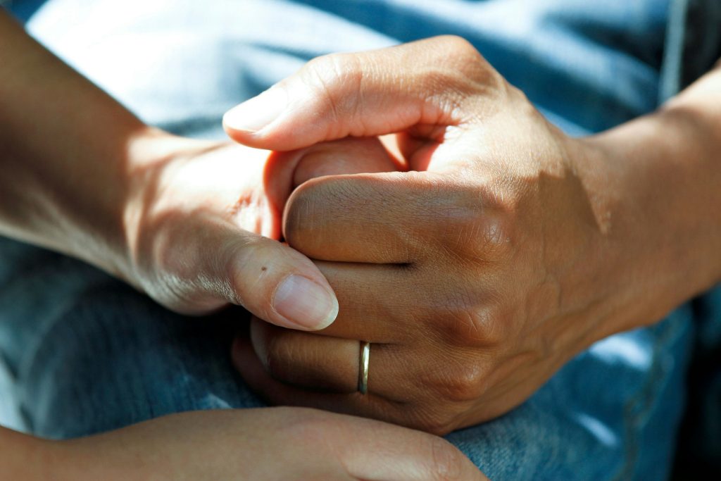 Close-up of two people holding hands, representing caregiving, emotional support, cognitive health, and compassionate care.