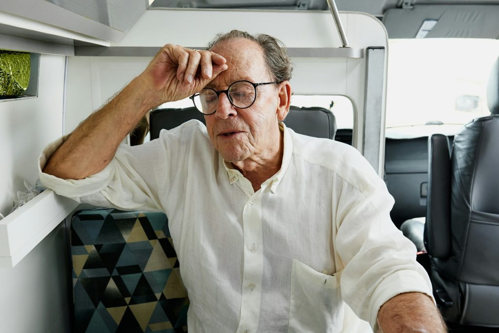 Older man sitting with his hand on his forehead, appearing tired or overwhelmed, illustrating fatigue, low energy, or reduced stamina.