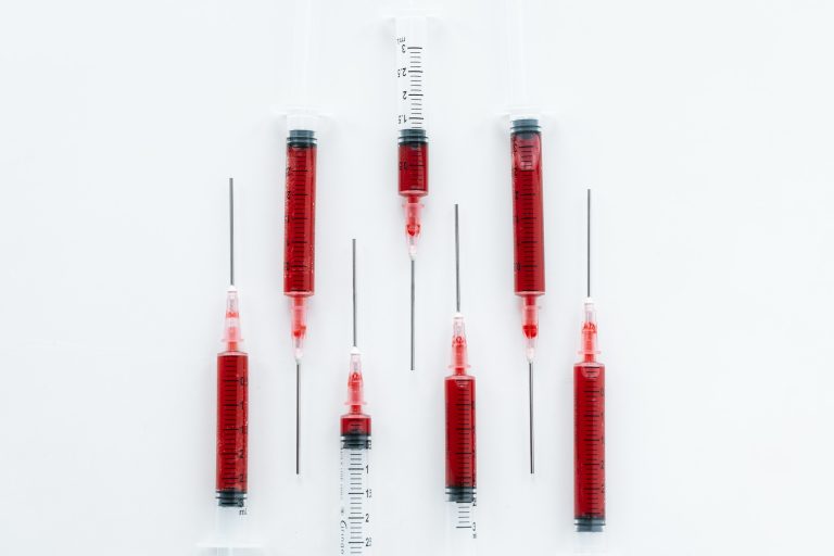 Several syringes filled with red liquid arranged vertically on a clean white background, representing injectable vitamin therapy and B12 injections.