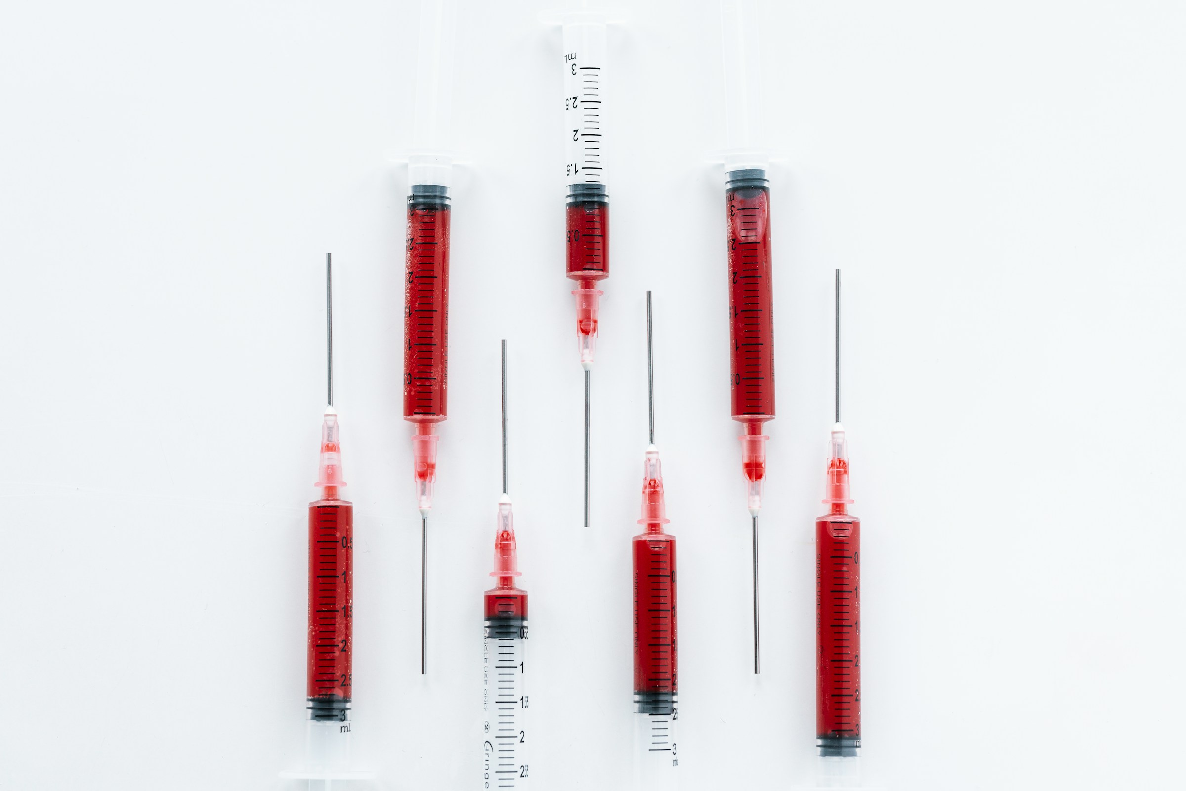 Several syringes filled with red liquid arranged vertically on a clean white background, representing injectable vitamin therapy and B12 injections.