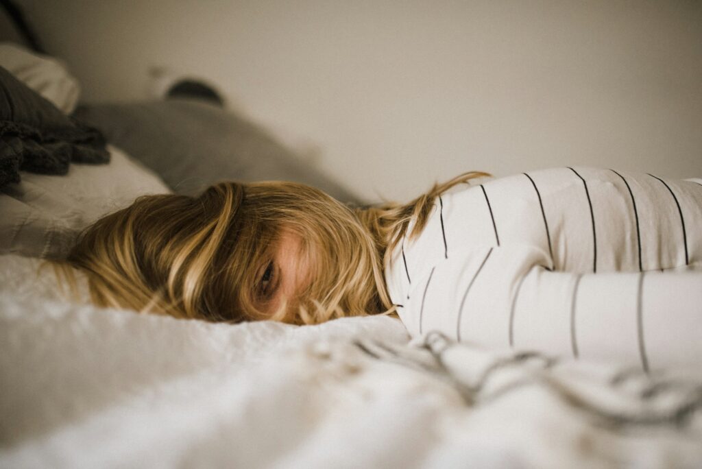 Person lying face down on a bed, appearing exhausted and unable to fully rest.